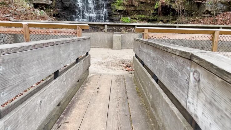 walking across a wooden bridge revealing a rushing blue and crystal clear waterfall and pond in cove spring park frankfort kentucky in 4k slo mo 60fps
