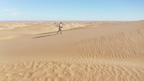 cinematic drone footage of a man walking in the desert with a camera, taking a photo of the landscape