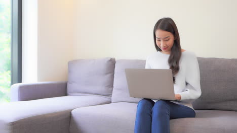 Joven-Asiática-Que-Trabaja-En-Línea-Desde-Casa-Usando-Una-Computadora-Portátil-En-La-Sala-De-Estar,-Fotograma-Completo-En-Cámara-Lenta