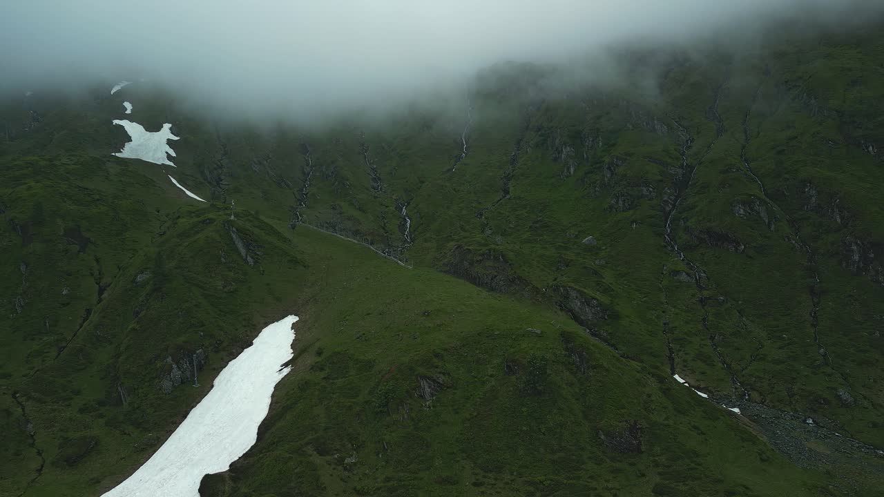 montañas verdes con manchas de nieve bajo una cubierta de nubes
