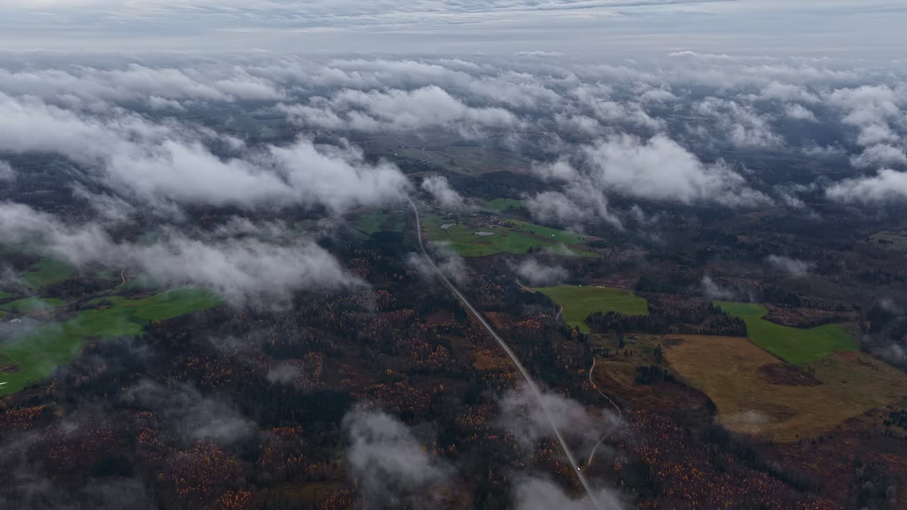 Timelapse aerial of low-hanging clouds moving above a rural autumn landscape and winding road