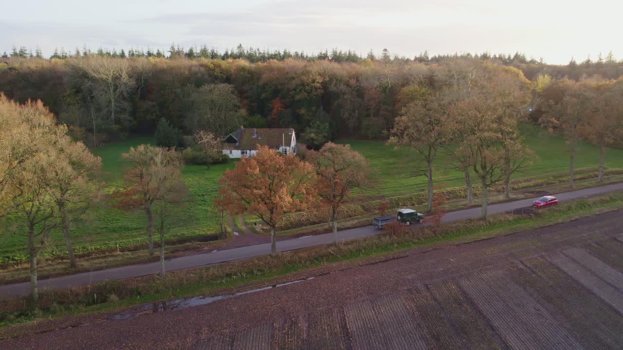 녹색 suv는 네덜란드에서 가을에 나무가 있는 작은 도로를 달린다.