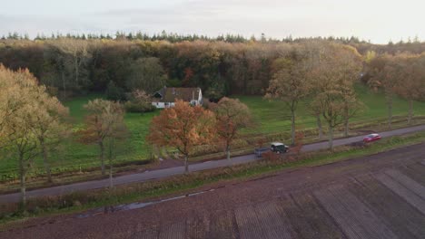 Green-SUV-drives-on-small-road-with-trees-during-autumn-at-the-Netherlands,-aerial