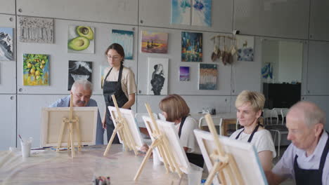 Vista-Lateral-De-Una-Gente-Mayor-Feliz-Sonriendo-Mientras-Dibuja-Como-Actividad-Recreativa-O-Terapia-En-Clase-De-Pintura-Junto-Con-El-Grupo-De-Mujeres-Y-Hombres-Jubilados