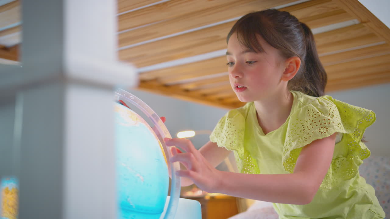 노트북과 함께 침대에 누워있는 침실의 소녀가 조명된 지구를 보고 있습니다.