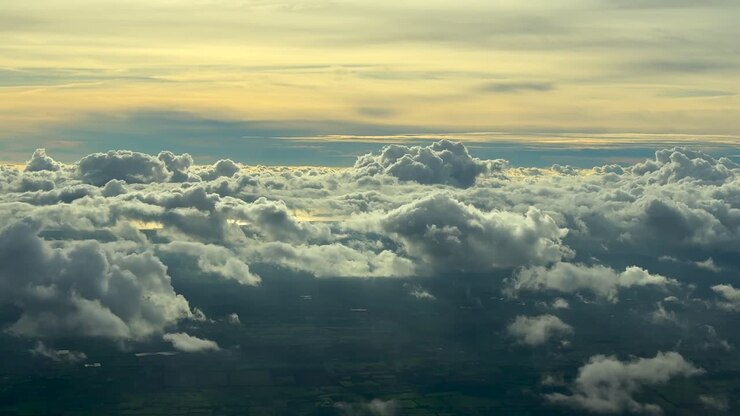 Pilot’s eye aerial view while flying over a broken layer of stratus clouds over a coastal landscape, with the scene bathed in the sunset light