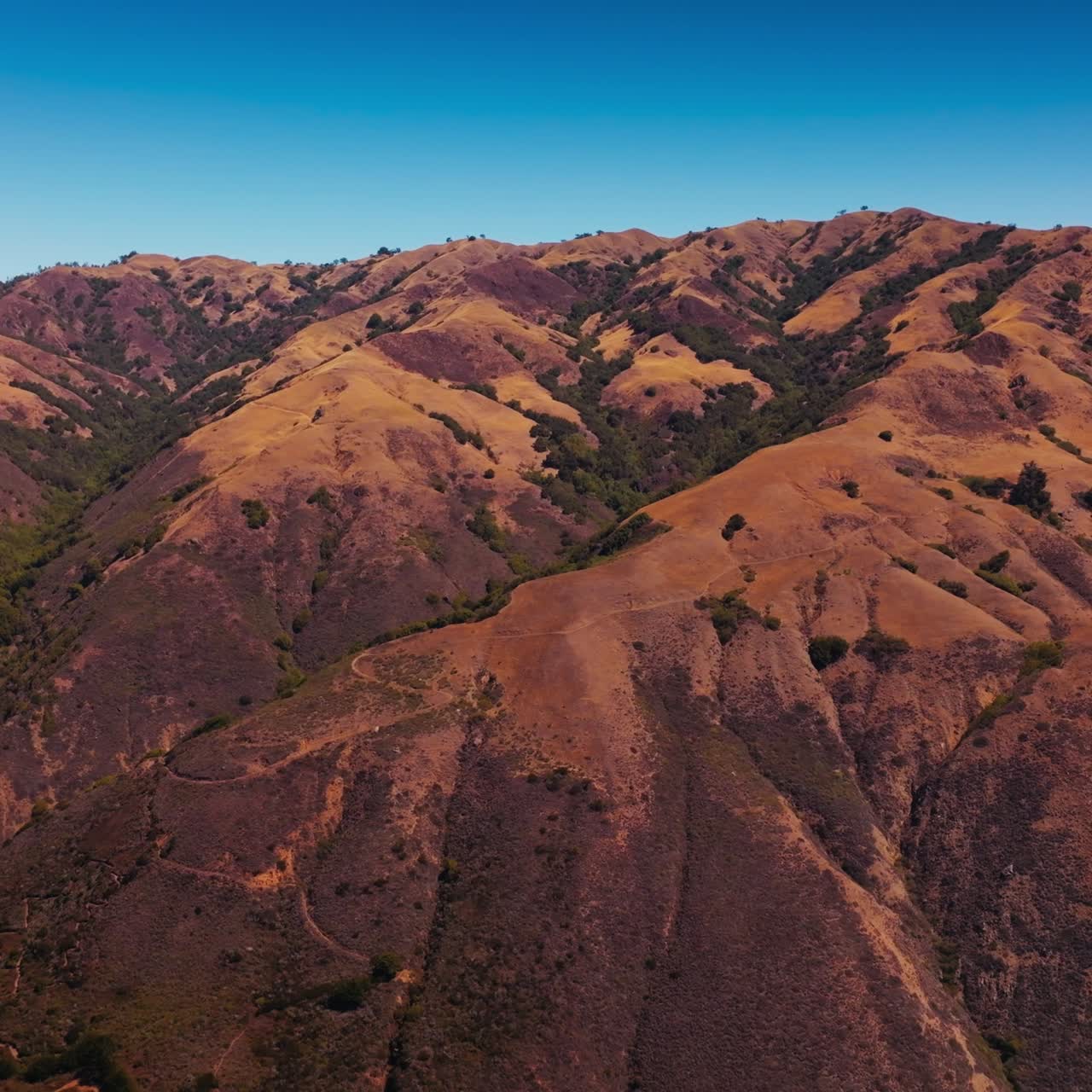 Rising above mountains, bare brown rocks with no vegetation, rock with moss. Rocky coastline of California at backdrop of blue clear sky. Aerial view