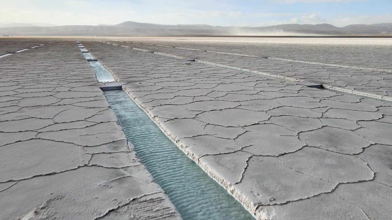 Shallow turquoise brine canals cut through cracked white salt crust on the Salinas Grandes in Jujuy, Argentina, showing lithium brine extraction in a high Andean desert.