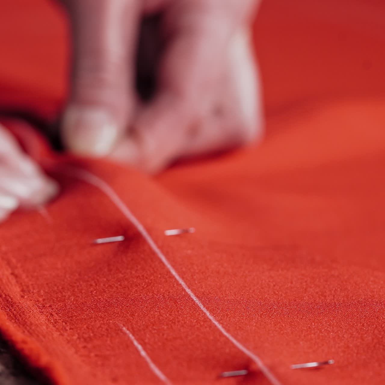 Professional seamstress puts the pins into the red fabric on the table. Woman's hands at work with red cloth and pins in the workshop. Close-up.