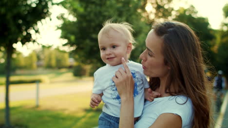 Toddler-with-mother-standing-on-street.-Smiling-woman-holding-boy-on-hands