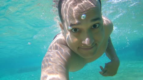 joven nadando en azul claro bajo el agua de la cascada con muchas rocas desde un ángulo plano