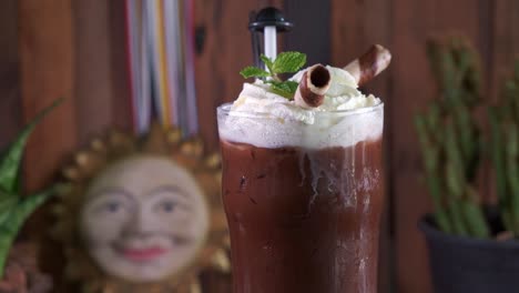 a fresh chocolate drink with whipped cram decorated with mint and chocolate straws spinning in a pint glass