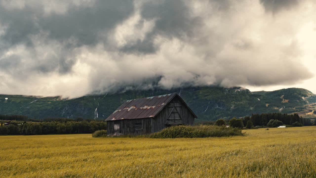 casa de granero abandonada asentada en un exuberante campo otoñal con gruesas nubes rodantes por encima de la toma amplia