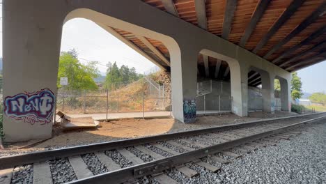 underpass with graffiti-covered pillars of cement and a railroad