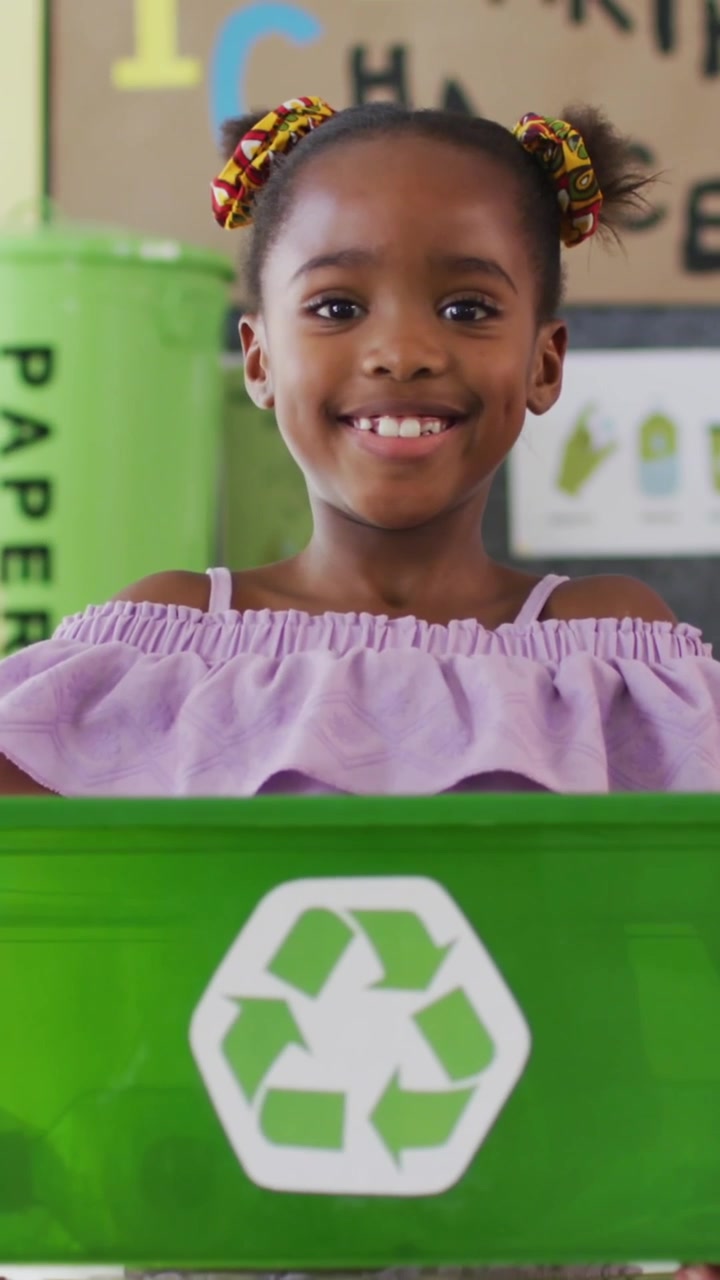Animação de sinais verdes de reciclagem sobre menina afro-americana segurando caixa de reciclagem verde