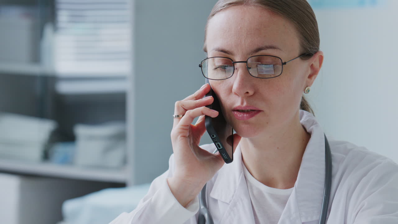 Female Doctor Speaking on Phone and Using Laptop in Medical Office