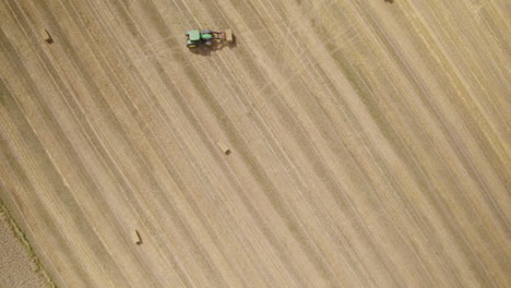 aerial top down of tractor collecting hay bales of farm field in sunlight,4k