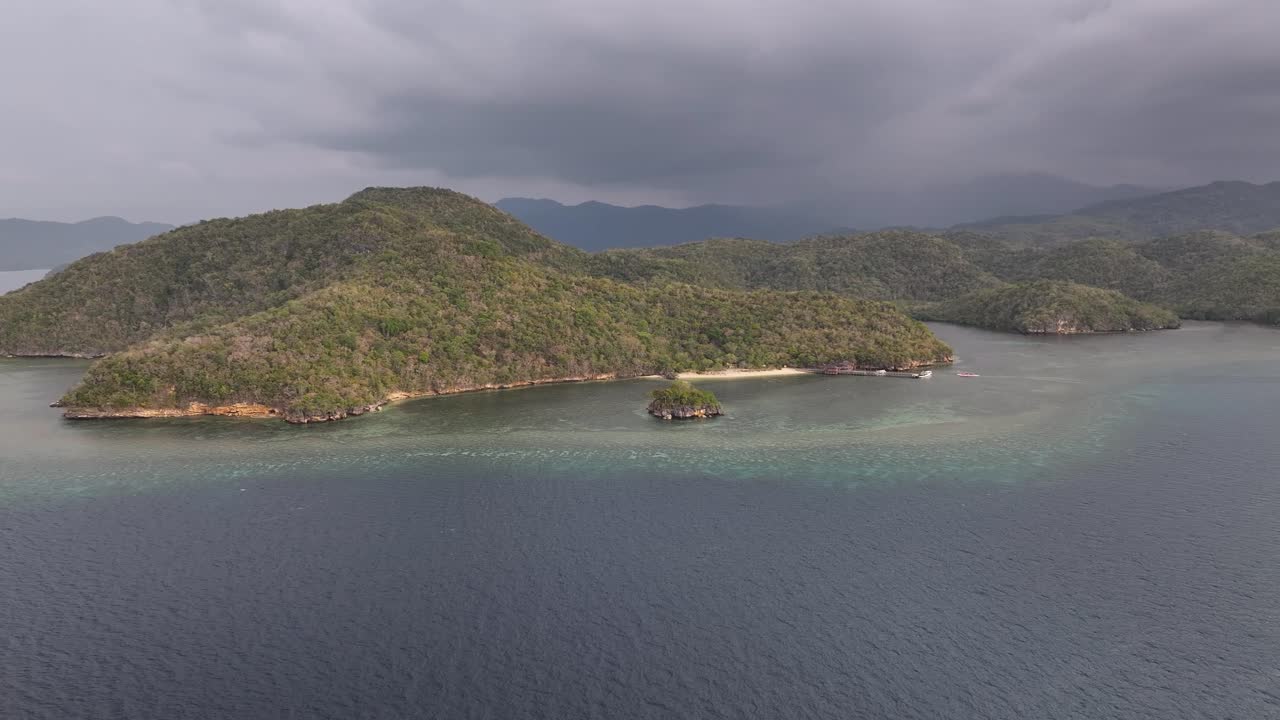 Rolling hills covered tropical vegetation and Rangko Cave tourist attraction seaside, Labuan Bajo, Indonesia.