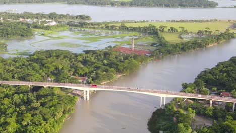 drone flying towards congrete brigde with traffic, connecting two forested areas, bangladesh