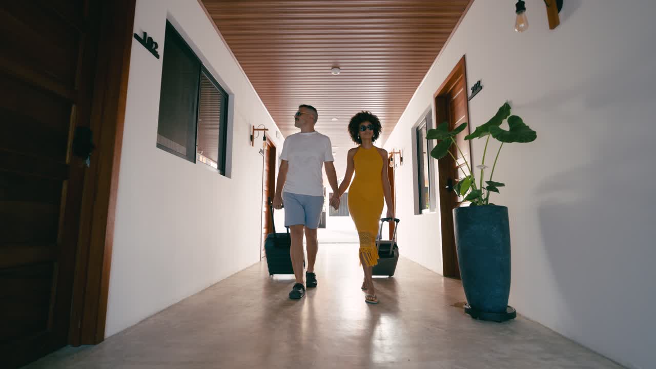 Happy Couple Walking Hand in Hand with Luggage in Hotel Hallway