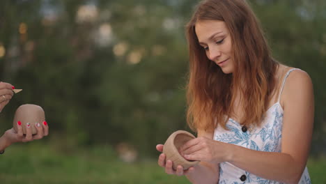 mujeres jóvenes forman un producto de arcilla aplican un patrón un dibujo en productos de arcilla con la ayuda de herramientas palos en un prado en la naturaleza en un espacio abierto. una mujer esculpe un primer plano.