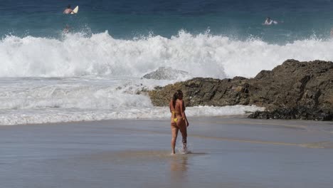 a woman walks through surf on a sunny beach day