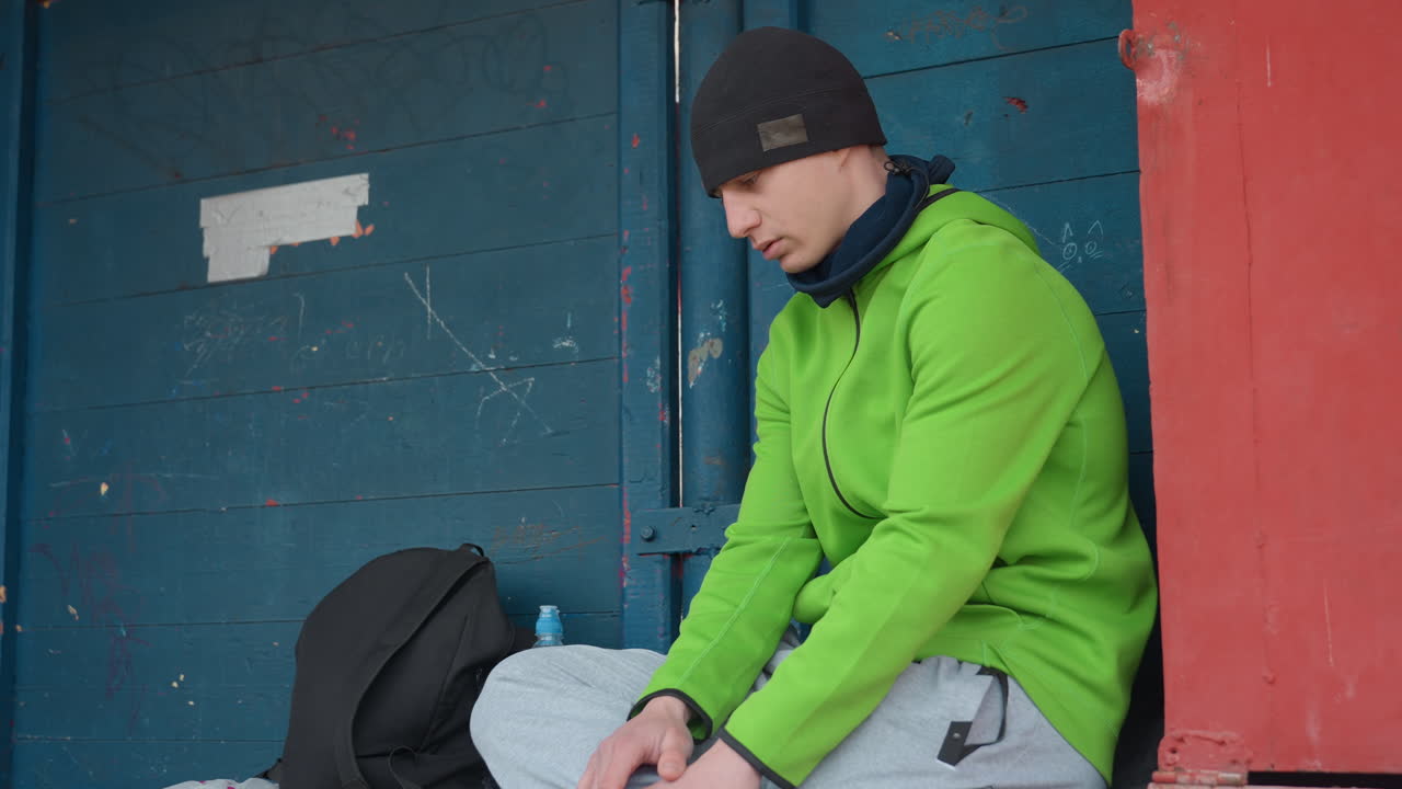 생각에 잠긴 남자가 쉬고 있어요. 사색에 잠긴 도시인이 벤치에 앉아 생각에 잠겨 있어요. яркий한 재킷을 입은 시민이 겨울 동안 야외 벤치에 앉아 숙고하고 있으며, неоново-зеленом 코트를 입은 남성 인물이 사색에 잠겨 앉아 있어요.