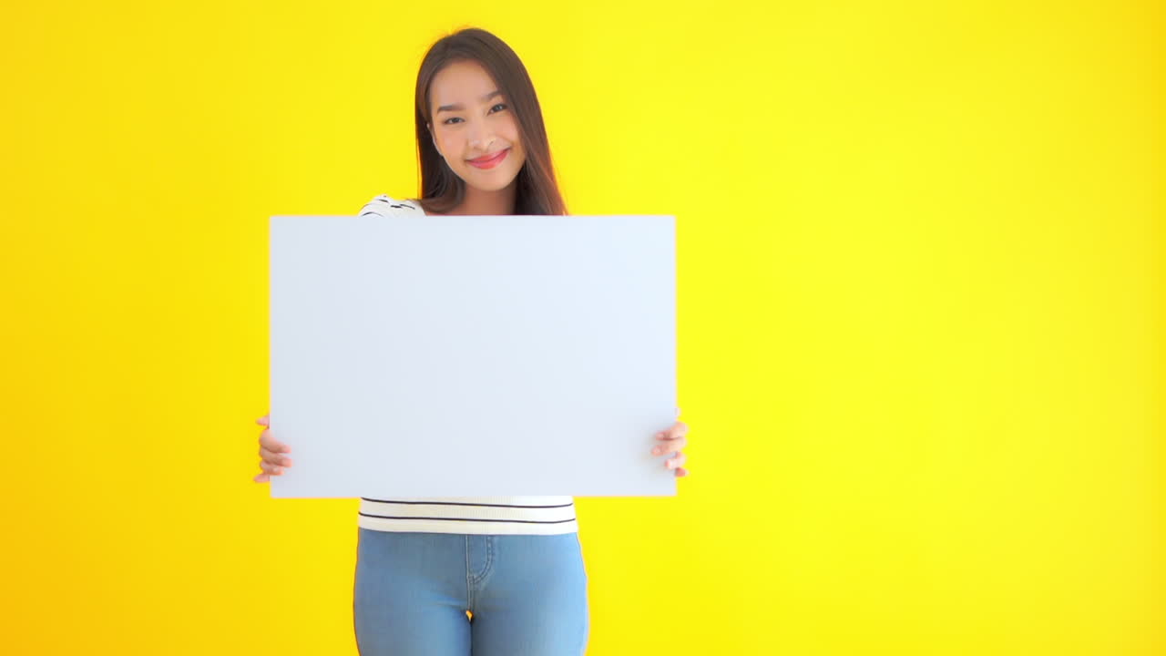 An attractive young Asian woman holds up a blank cardboard sign. Copy space
