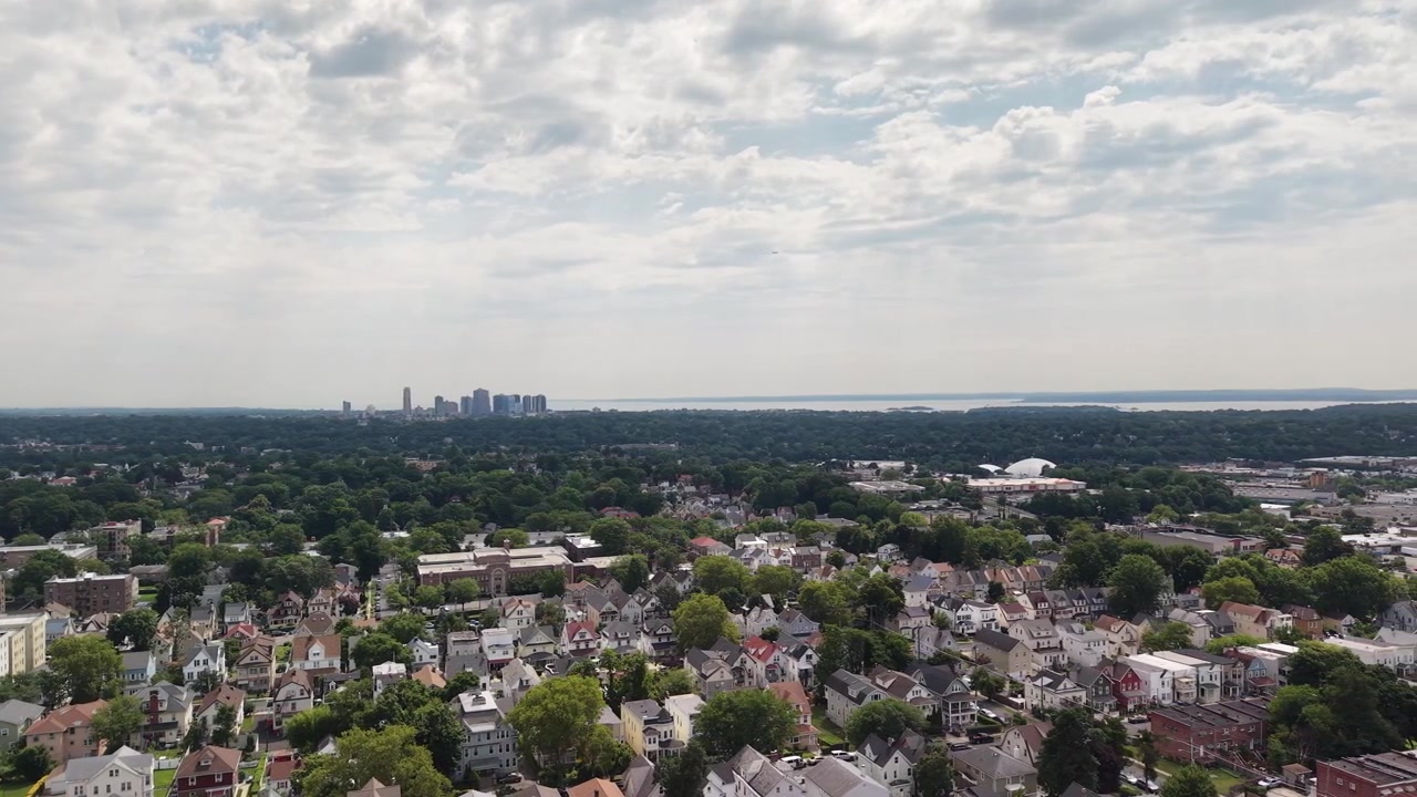 Ampia vista aerea che si muove lentamente in avanti su un quartiere residenziale a New Rochelle, New York, rivelando lo skyline del centro e il Long Island Sound in una giornata parzialmente nuvolosa