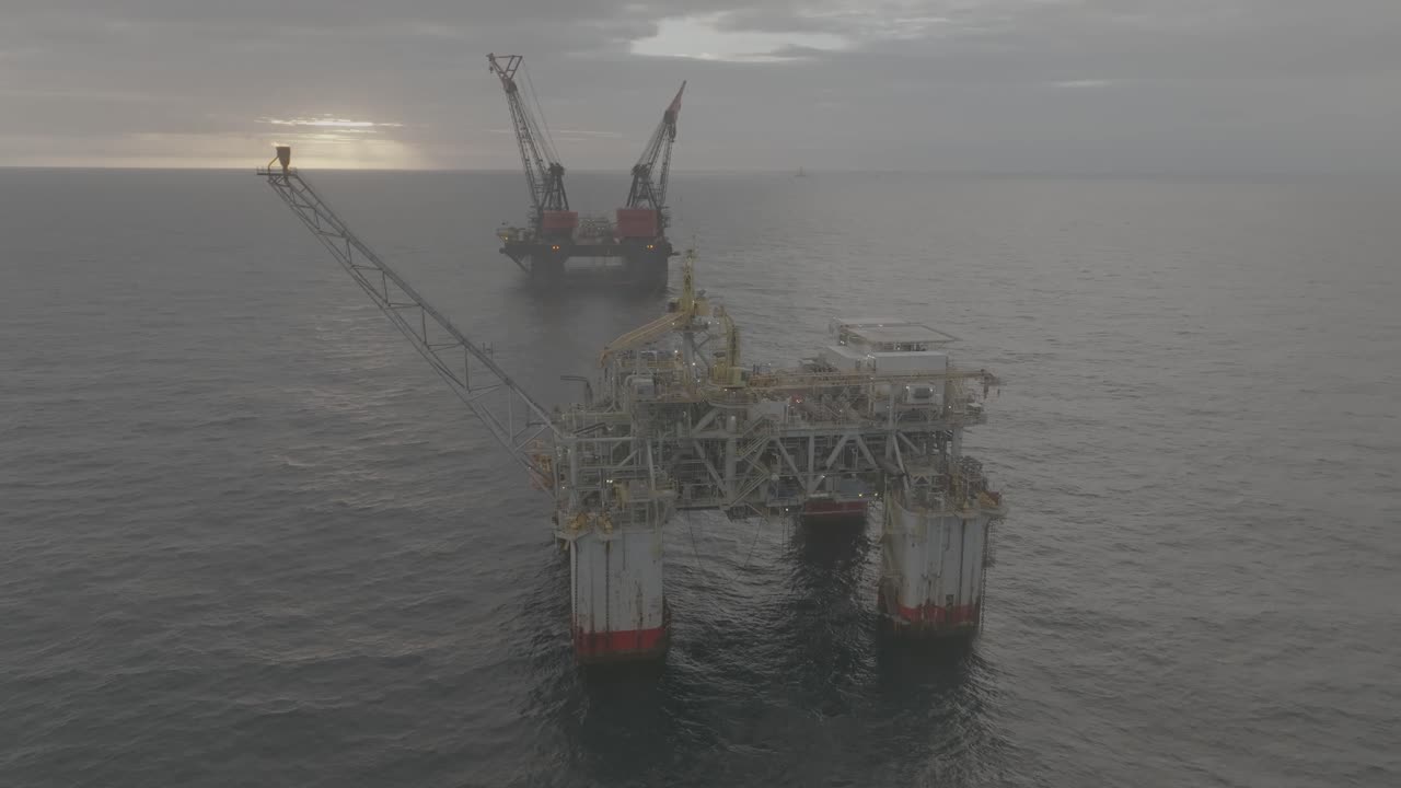 Droneoptagelse af en offshore olieplatform og et kranskib ved solopgang over havet