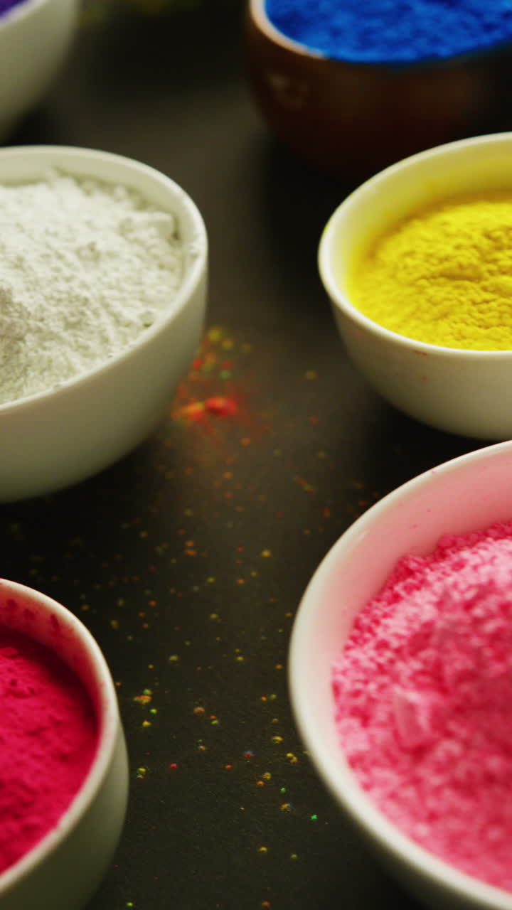 Vertical video of bowls of colourful powders on black background, with copy space