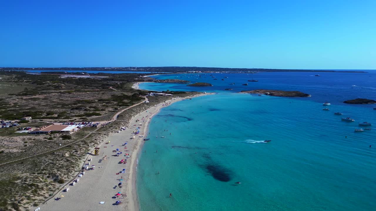 Spiaggia di Platja de Ses Illetes a Formentera con un oceano blu turchese cristallino e persone che si rilassano sotto un cielo terso. Perfetta vista aerea, volo in retromarcia, panoramica generale con drone
