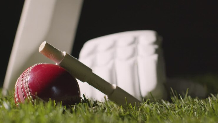 Natura morta di cricket con primo piano di mazza, palla, bails e guanti adagiati sull'erba 1