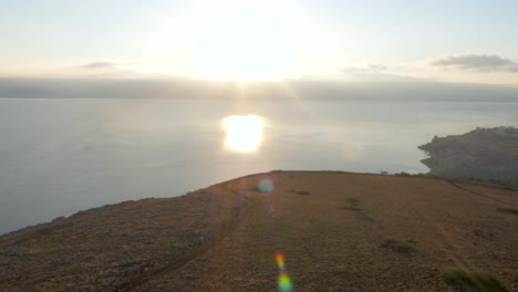 vista aérea de drones, movimiento hacia adelante: dejando la tierra y volando sobre el mar, hacia el sol brillante