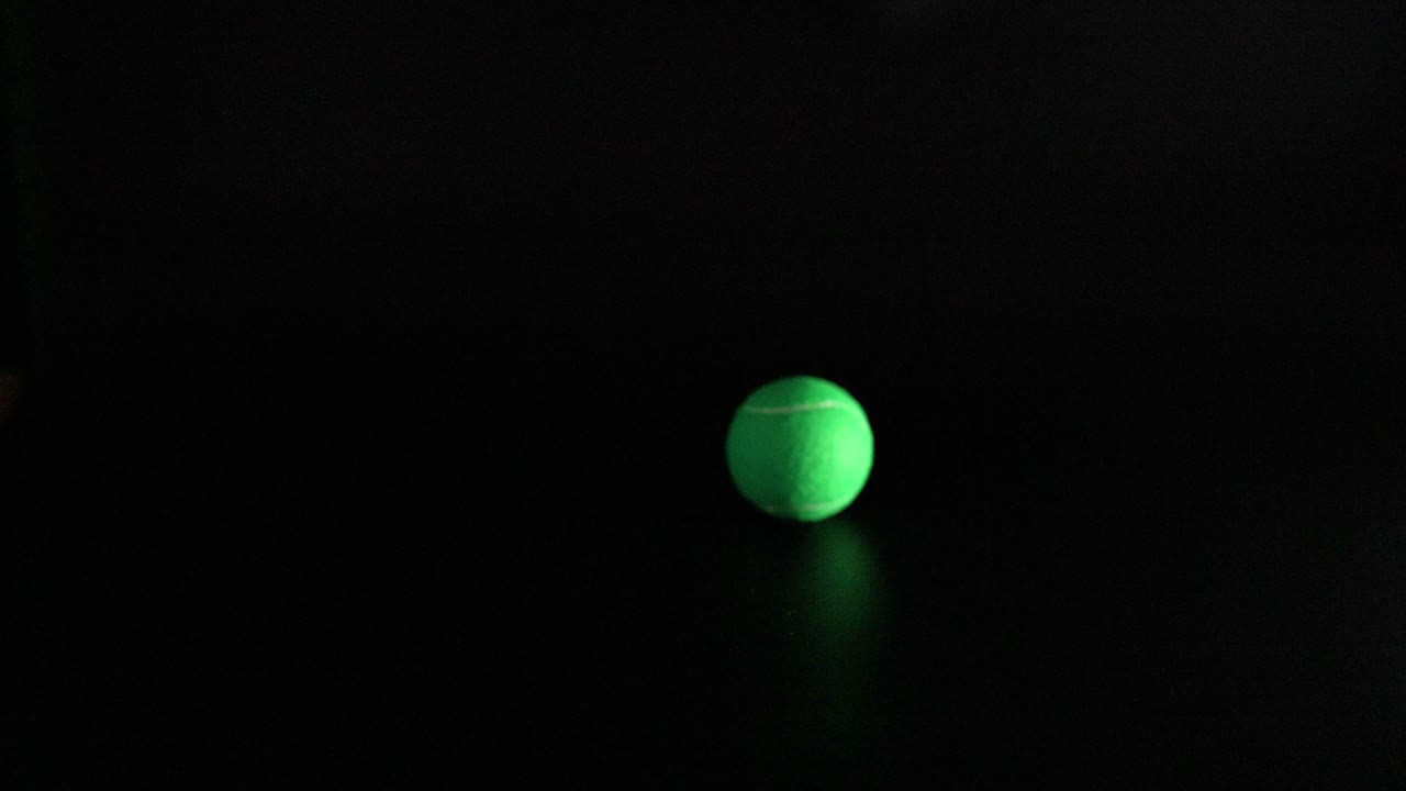 A tennis ball bounces in a dark environment