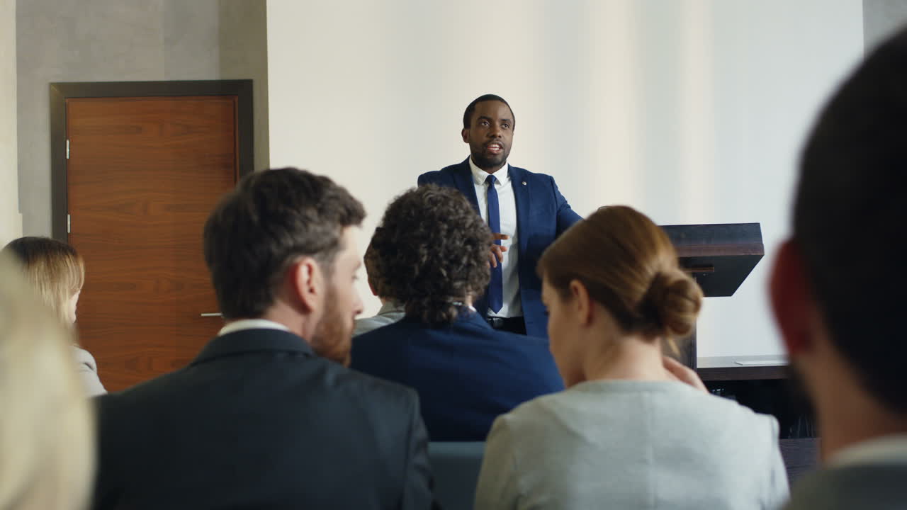 African American young businessman wearing formal clothes speaking at the conference in front of the many people