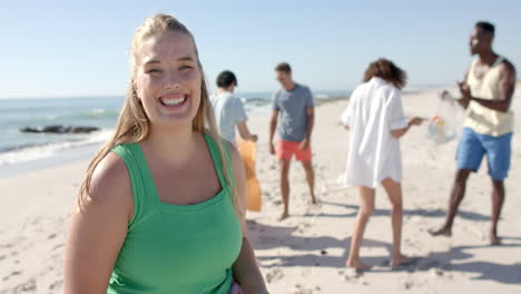 jovem mulher caucasiana sorri na praia enquanto recolhe lixo, com espaço para copiar