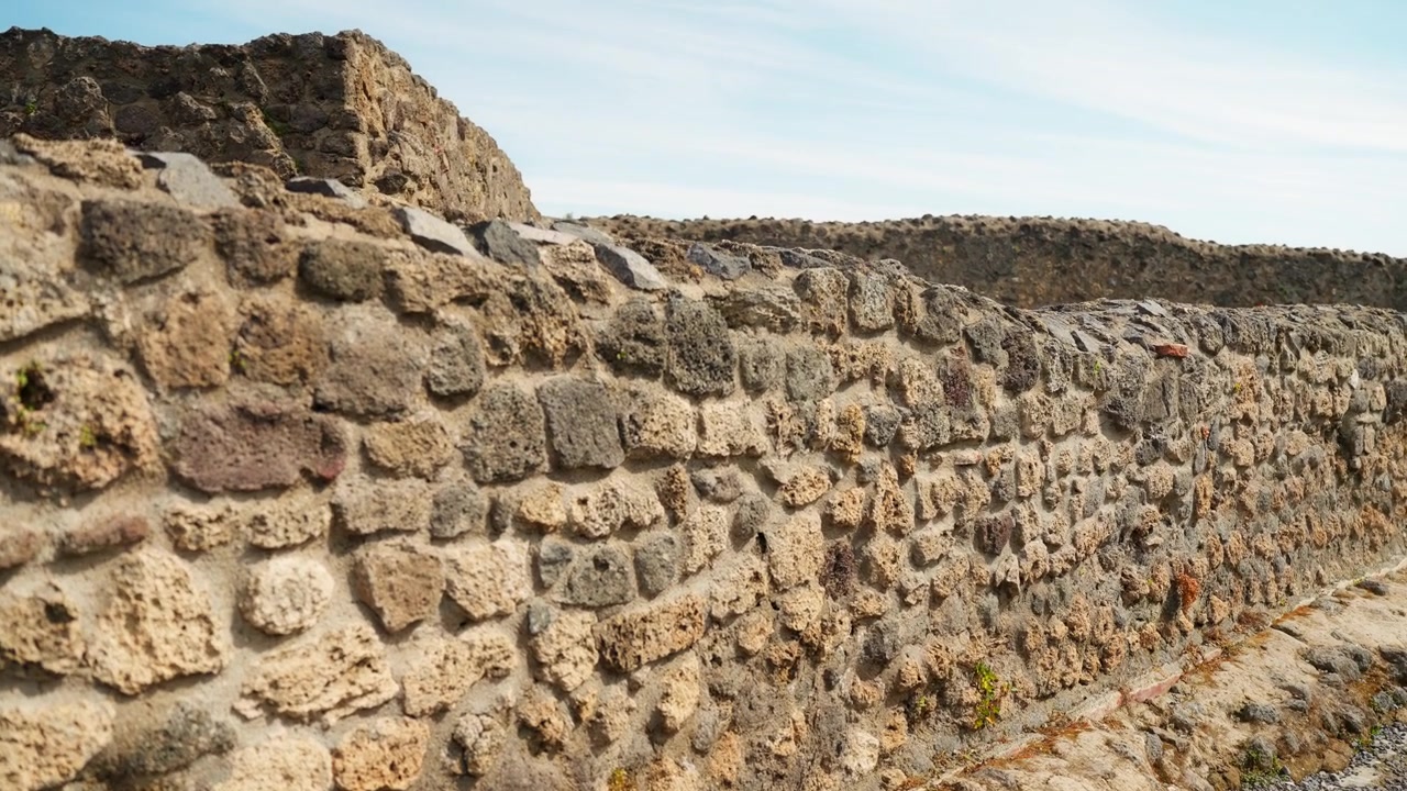 Vista ravvicinata di un muro grezzo di Pompei accanto a un sentiero di ghiaia, che mostra pietre vulcaniche, malta, muratura stagionata e la texture di un'antica rovina romana