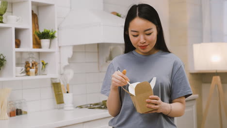 feliz chica japonesa comiendo ramen para llevar mientras mira a la cámara y sonríe