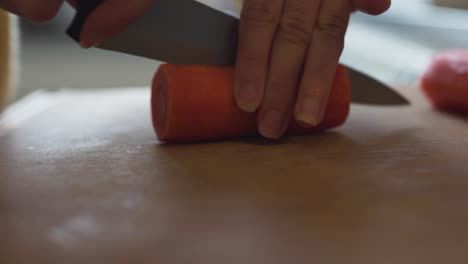 primer plano de una mujer en una cocina usando un cuchillo afilado para cortar una zanahoria en pedazos-1