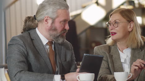 Ältere-Geschäftspartner-Nutzen-Tablet-Und-Unterhalten-Sich-Im-Restaurant