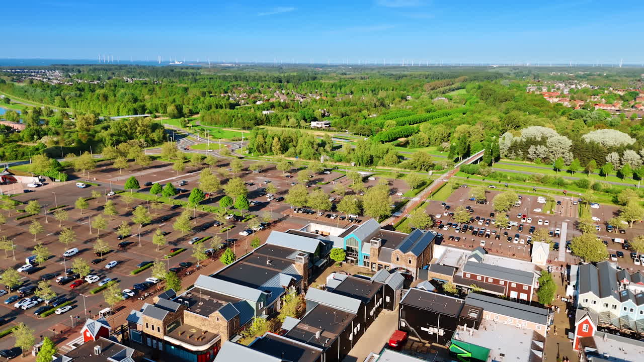 Flying over the private houses in Lelystad, the Netherlands. Large parking lot with trees growing on surrounds the residential area. Lush green forests or park at backdrop.