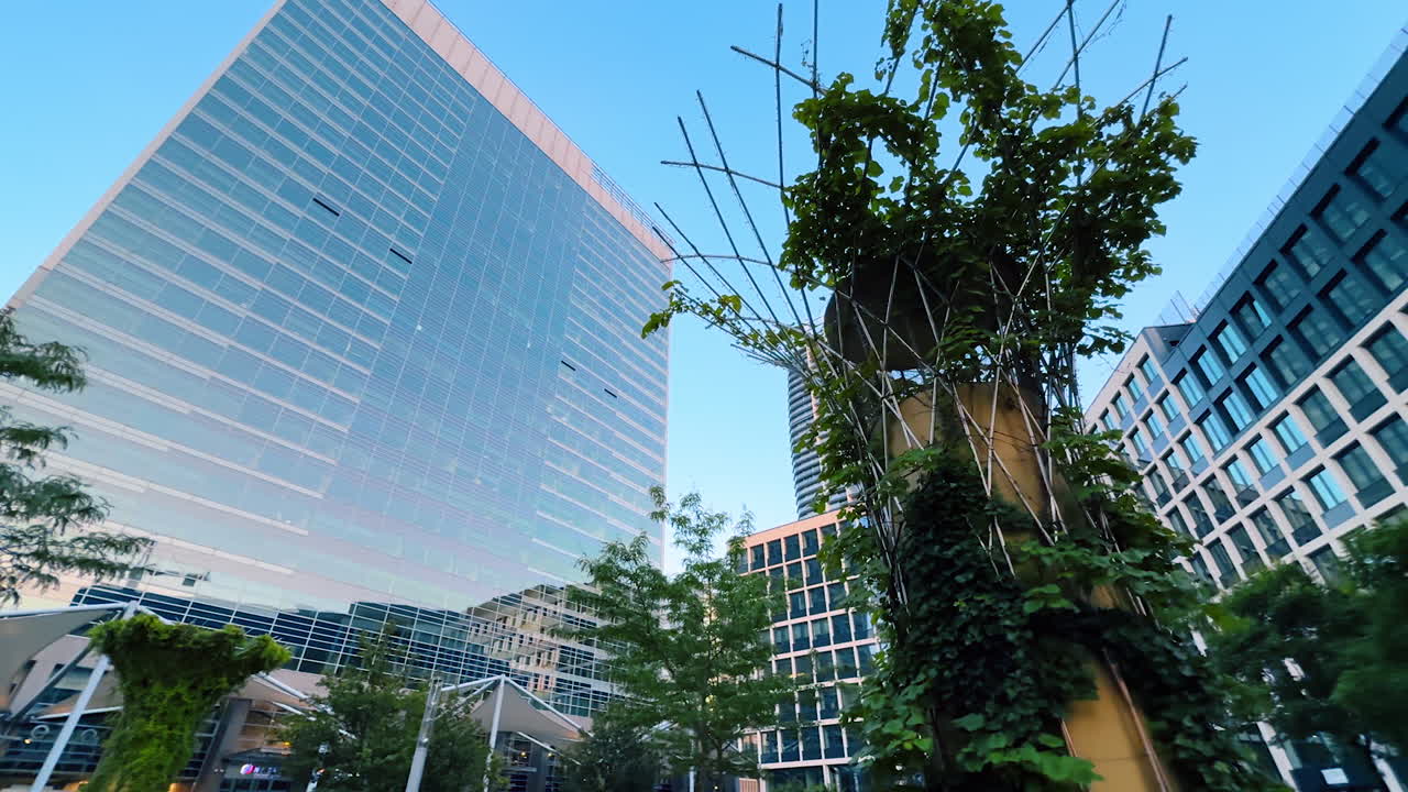 Bratislava, Slovakia - June 5, 2025: Greenery-surrounded office building. An urban office structure rises against a clear blue sky, accented by lush plants and trees in the foreground