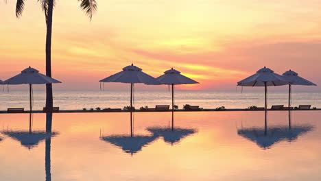 a dramatic view from a resort pool of a sunset of pink, yellow, and orange hangs over the ocean horizon