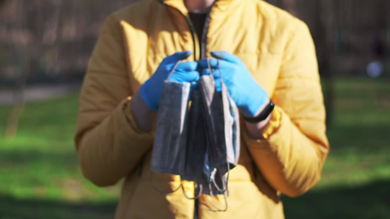 Man in medical gloves holding a bunch of dirty medical masks raised from the ground. Pollution idea
