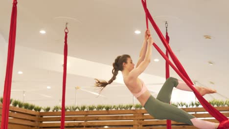 a beautiful gymnast does gracious maneuvers standing in the air on red ribbons