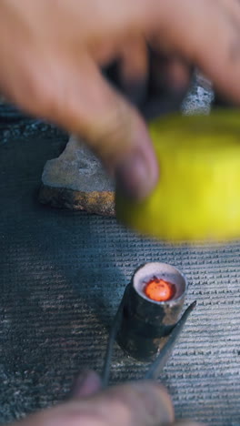 cu: experienced worker shapes heated with flame metal bar using yellow form stamp on asbestos sheet at workplace close view
