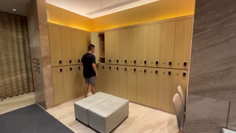 asian millennial man taking shirt off and hanging in locker in luxurious changing room