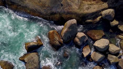 Aerial-top-down-shot-of-hypnotic-waves-breaking-on-the-boulders-at-the-coastline