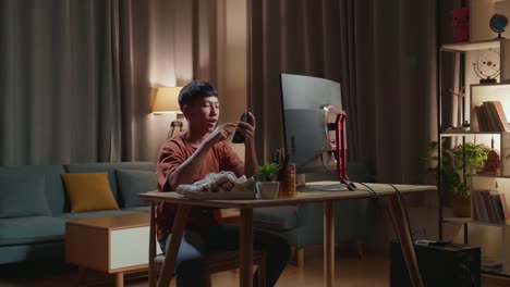 asian boy footwear designer using smartphone while working on a desktop computer at home